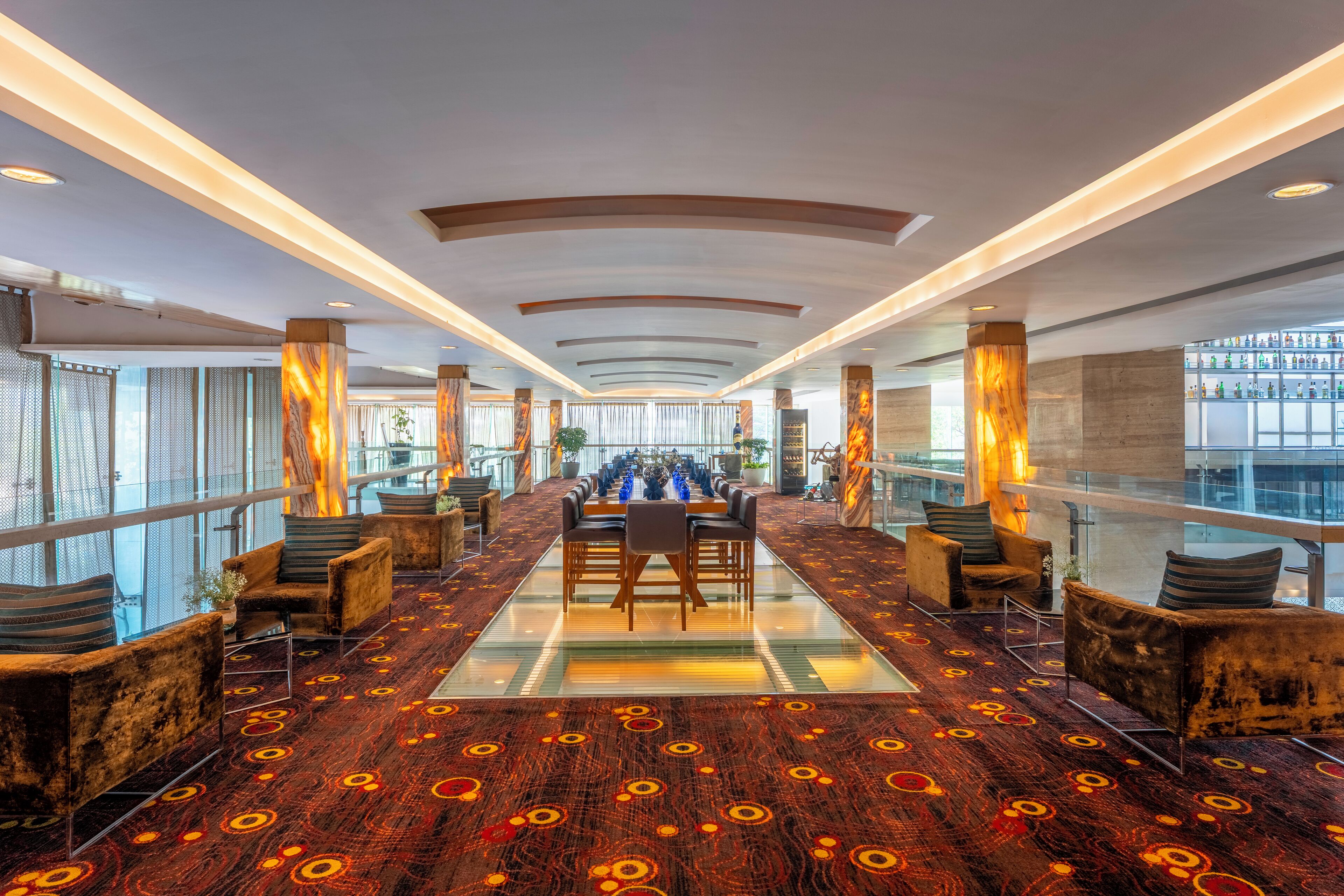 A spacious lobby with a long table and chairs, large windows, and a patterned carpet.