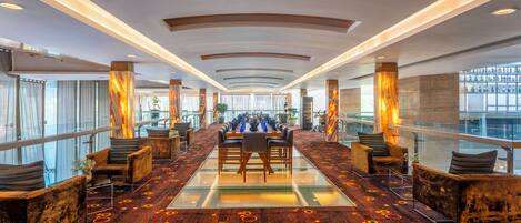 A spacious lobby with a long table and chairs, large windows, and a patterned carpet.