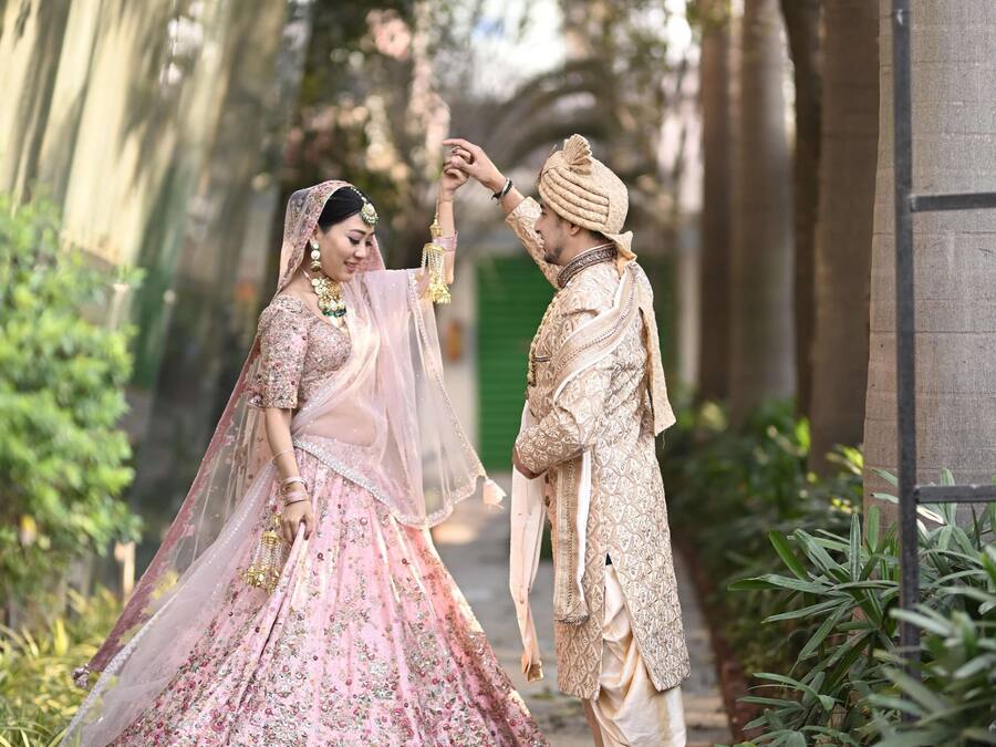 A couple in traditional wedding attire walking down a pathway lined with greenery.