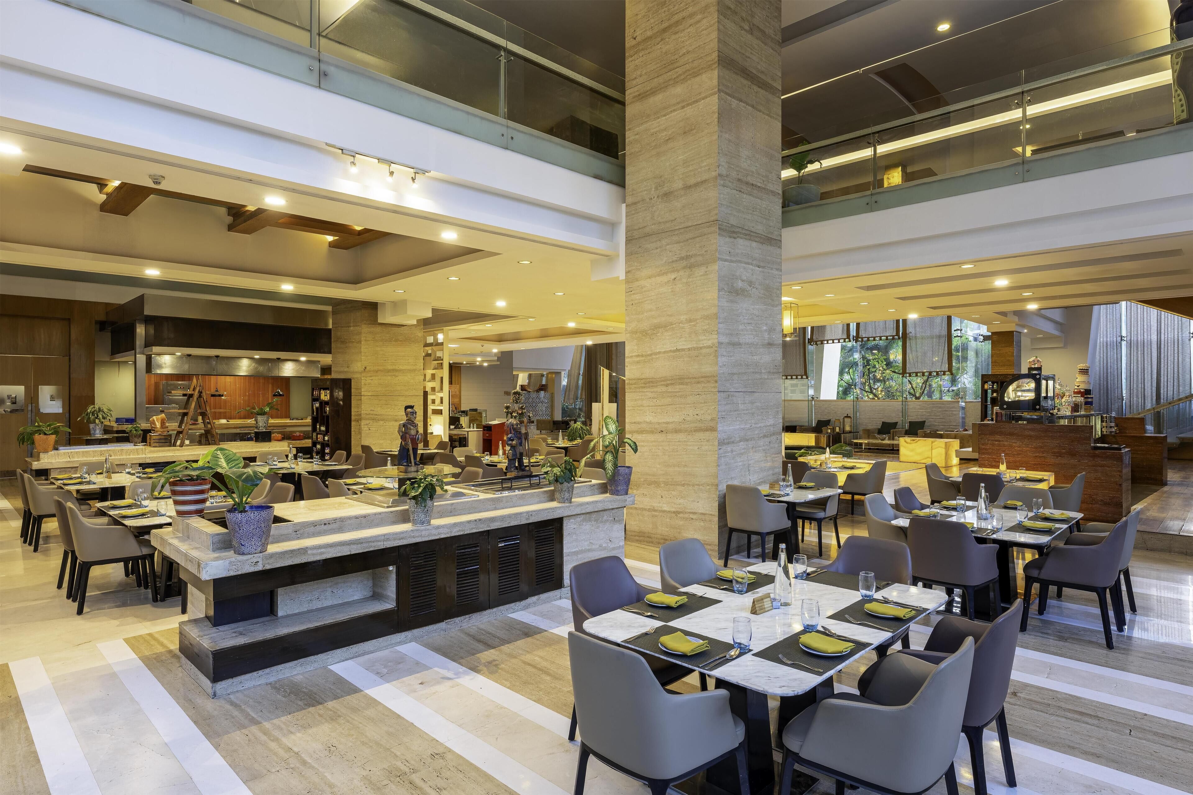 Un vaste espace de salle à manger moderne, doté de hauts plafonds, d’un îlot central avec des sièges et d’une cuisine en arrière-plan.