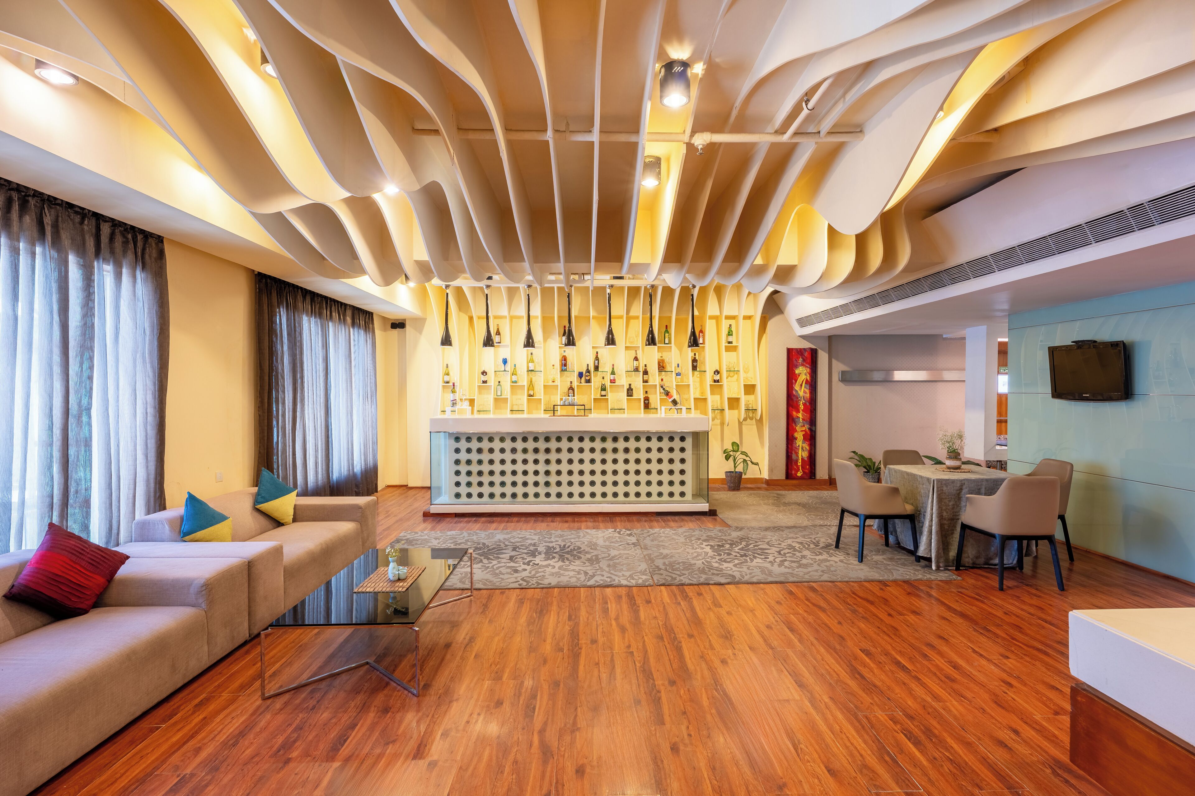 A modern living room with a sofa, a coffee table, a dining area with chairs, a patterned rug, and a wall with a decorative panel.