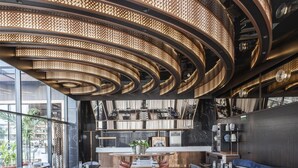Um restaurante moderno com uma mesa comunitária alongada, tetos altos com luminárias circulares e vista para o exterior.