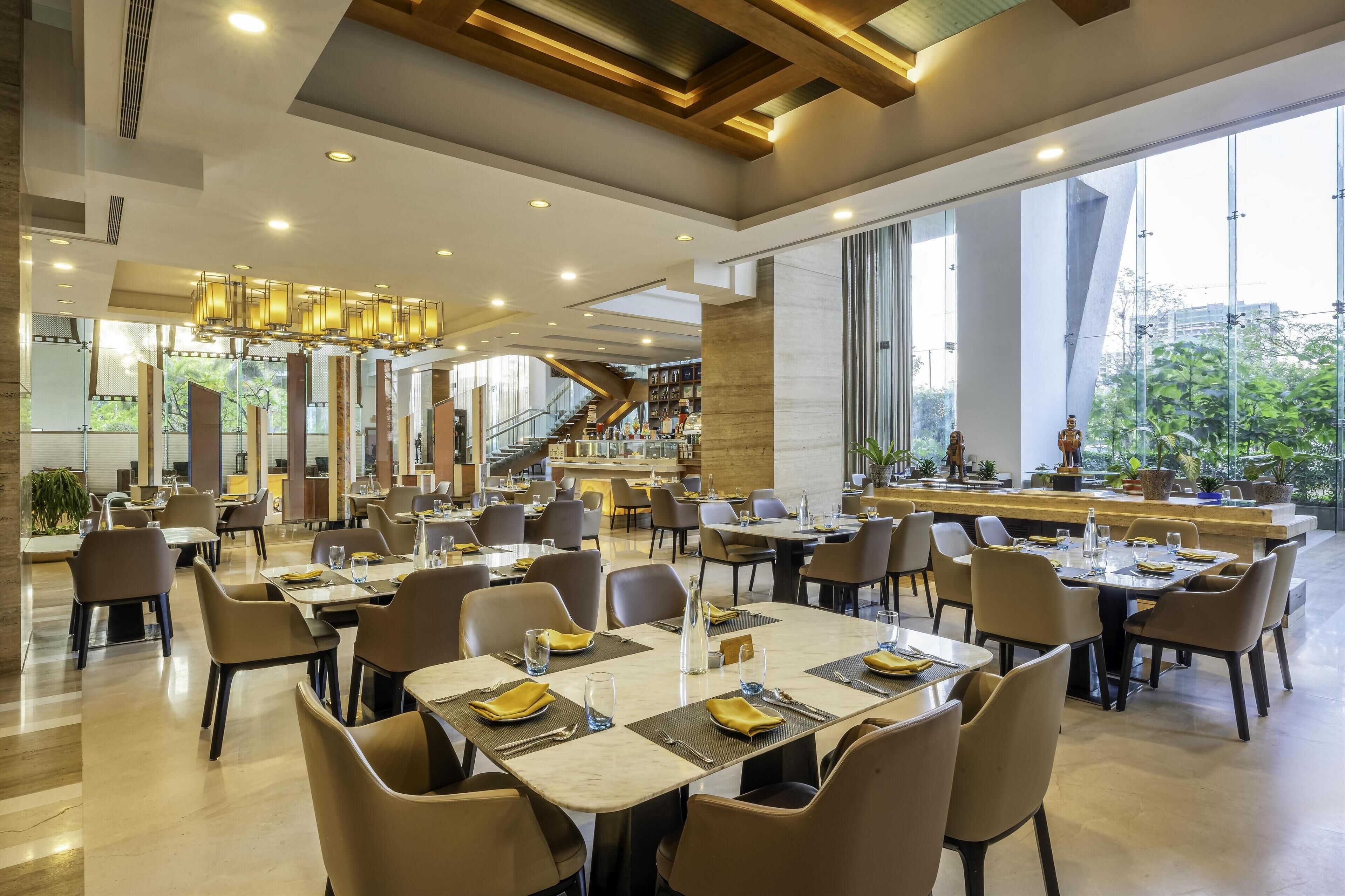 Un espace de restauration moderne avec des tables dressées pour les clients, un bar central et un escalier menant aux étages supérieurs.