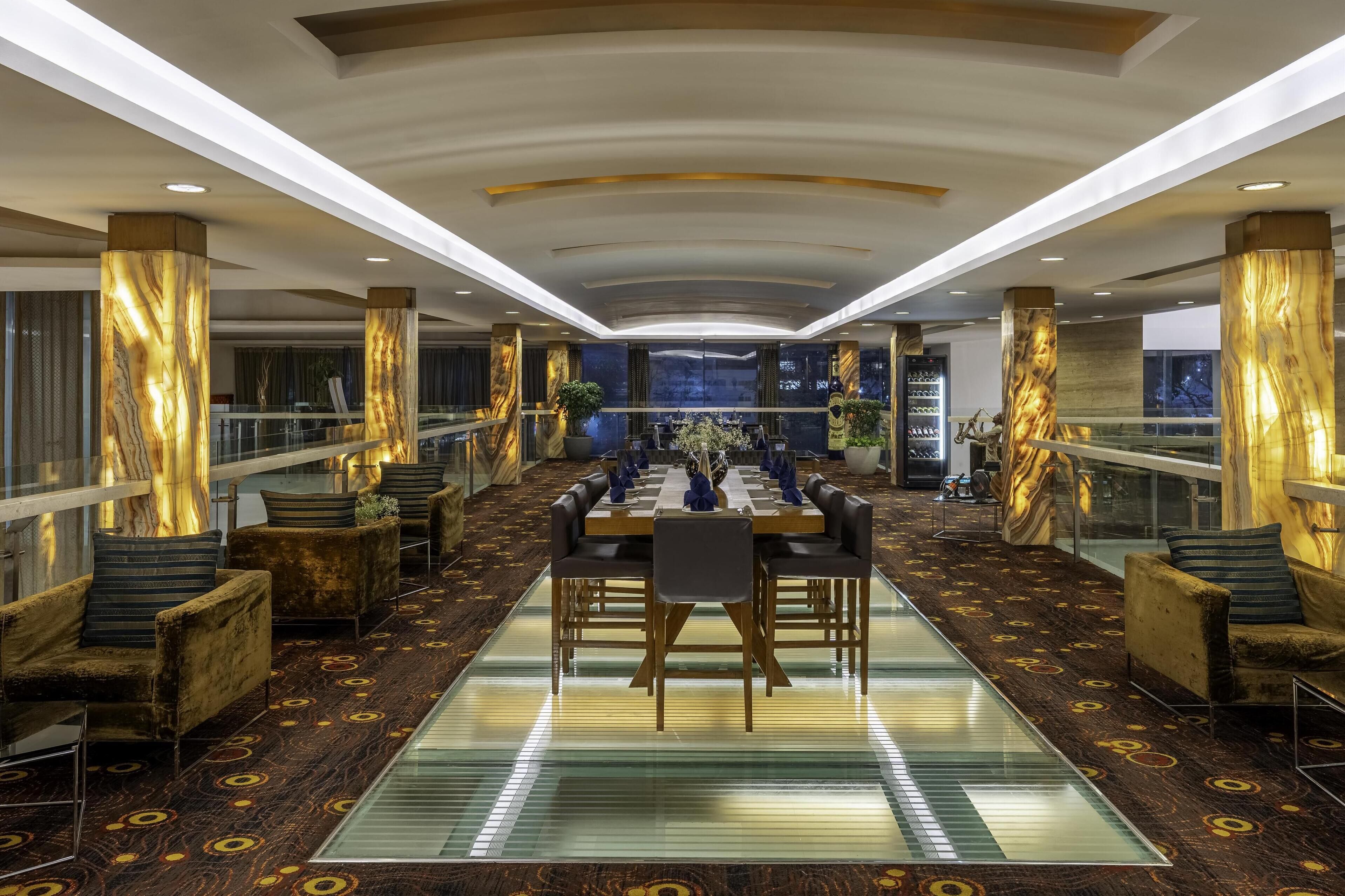 A spacious lobby with a long table and chairs, marble columns, and a patterned carpet.