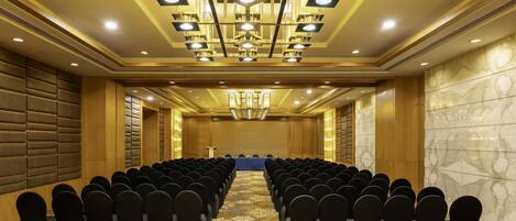 A conference room with rows of black chairs, a blue table, and a chandelier.