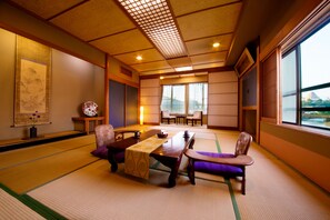 Una habitación japonesa tradicional con suelo de tatami, una mesa baja y sillas, un separador shoji y vistas a un templo a través de amplios ventanales.