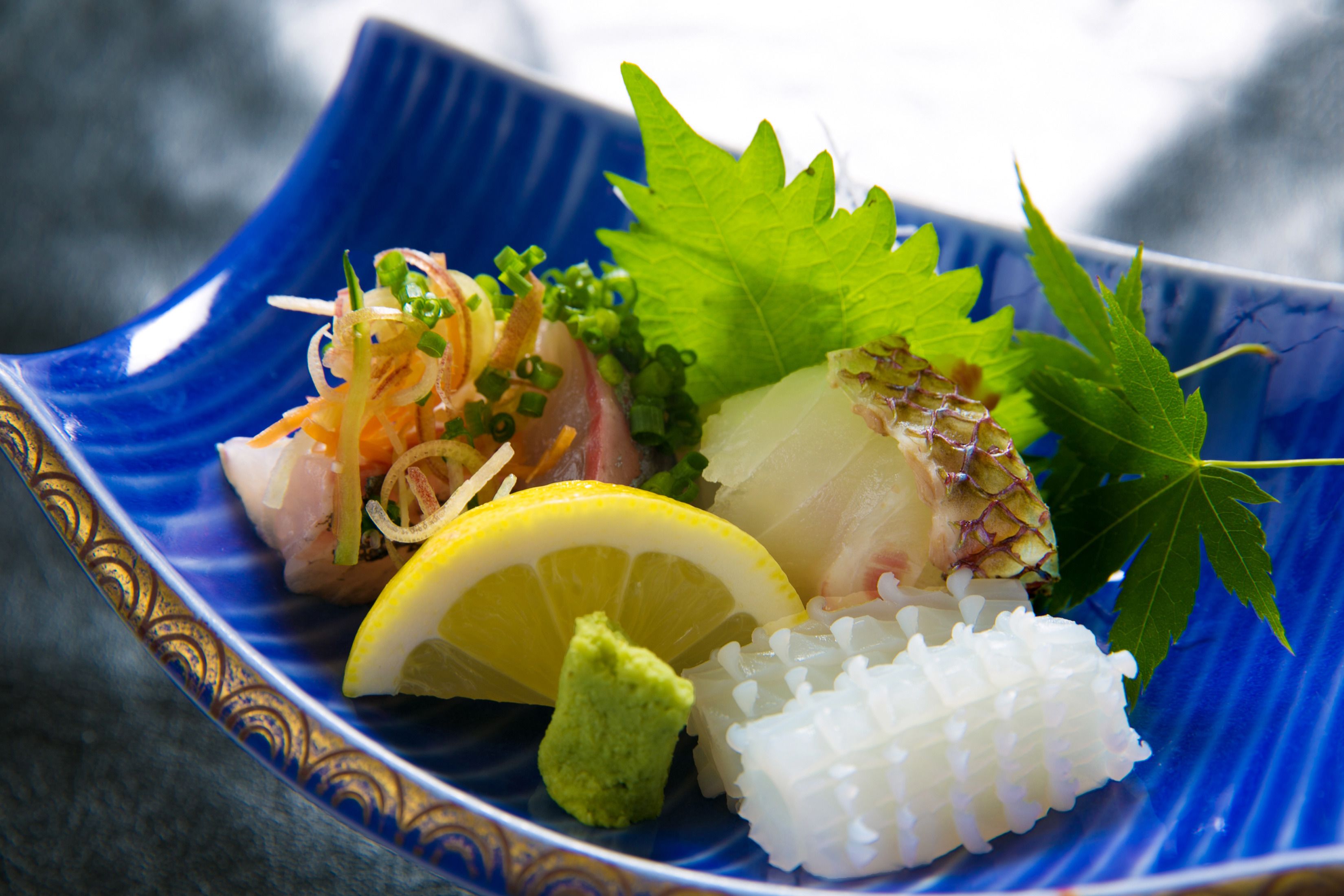 A blue ceramic dish with sushi, including sashimi, rice, and garnishes.