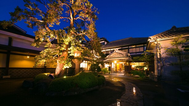 A traditional Japanese building with a stone pathway leading to the entrance, surrounded by well-maintained greenery and illuminated by warm lighting. - Ryokan Wataya (Karatsu)