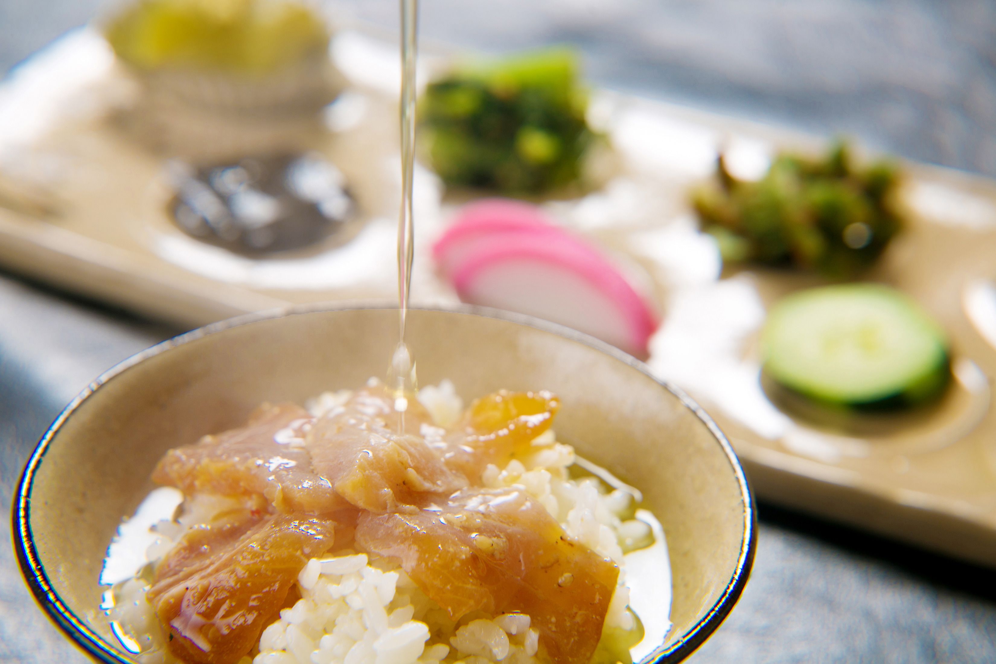 A bowl of rice with a sauce being poured over it, with other dishes in the background.