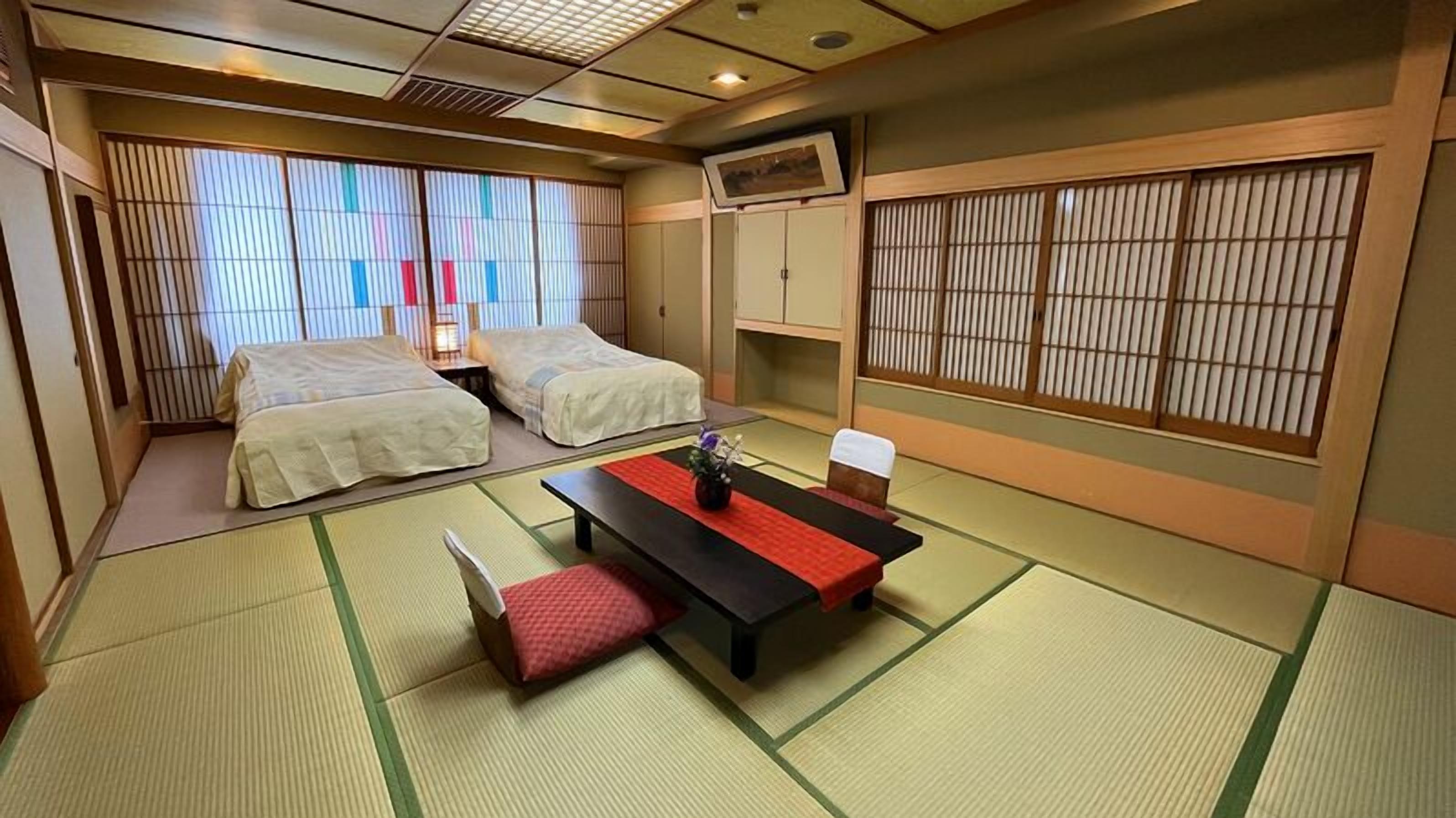 A traditional Japanese-style room with tatami flooring, two beds, a table with a vase, and sliding doors.