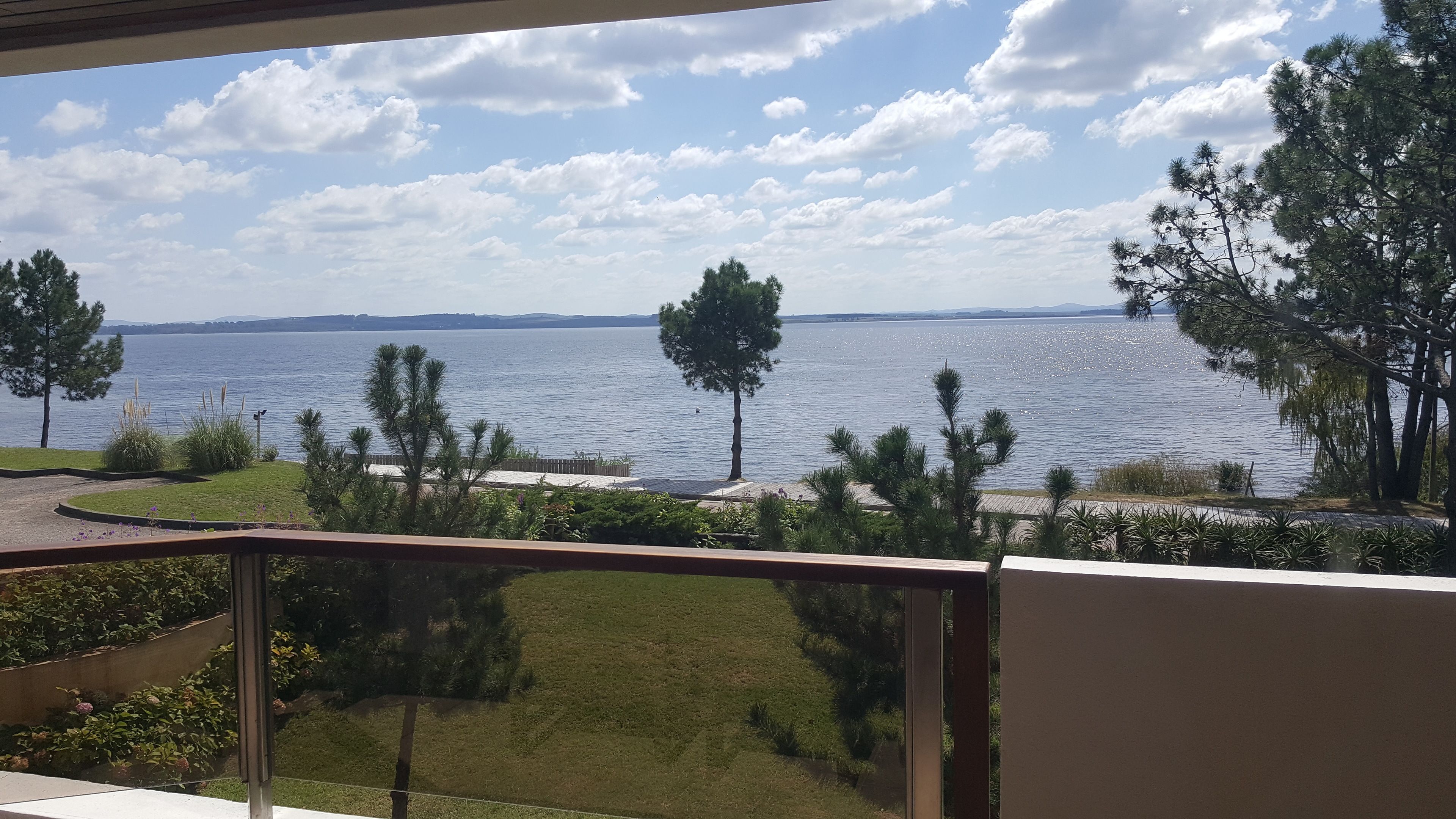 Un balcón con vistas a un lago, rodeado de árboles y una zona verde.