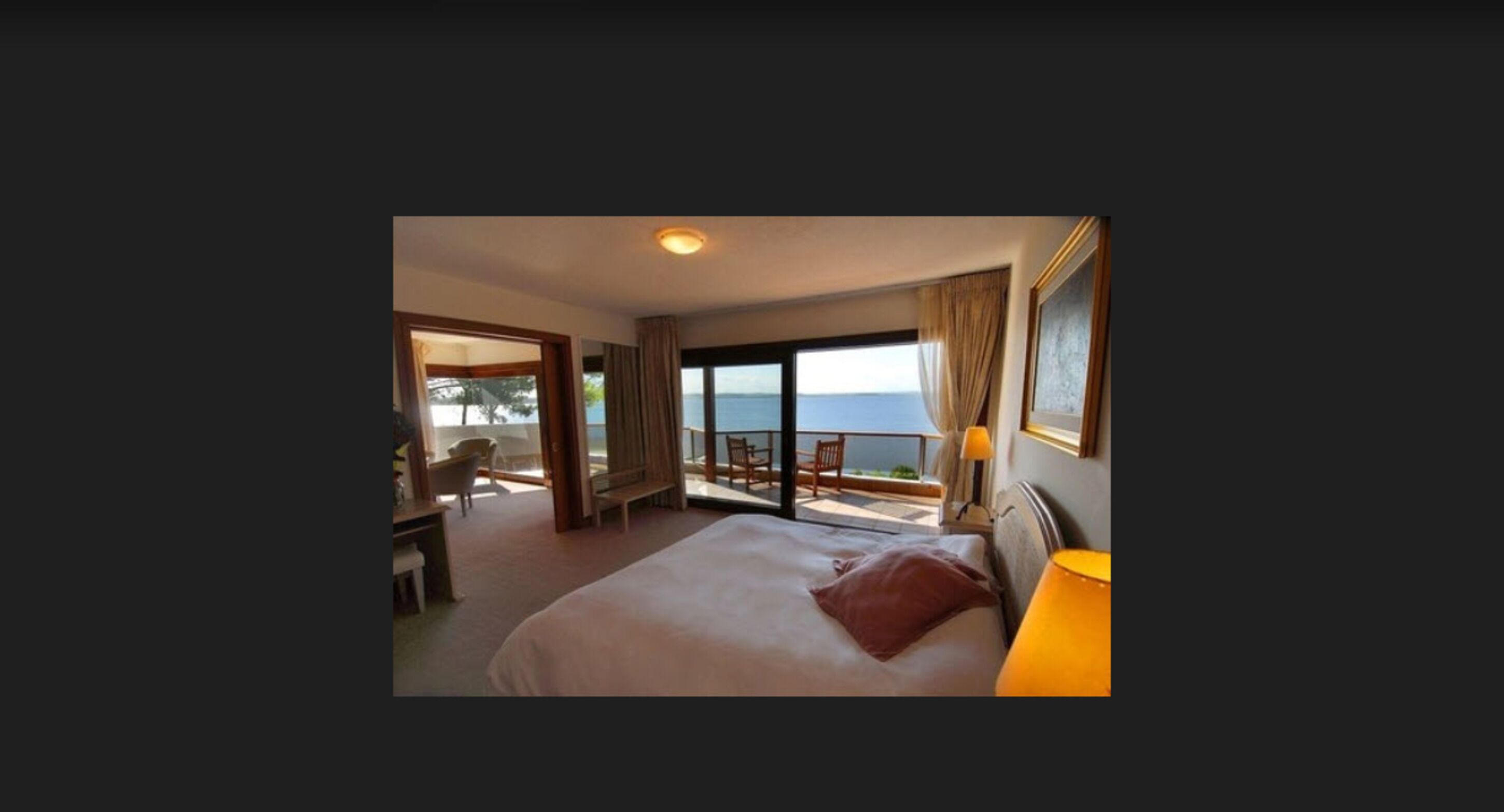 Habitación de hotel con una cama grande, un escritorio, una silla y vista al mar.