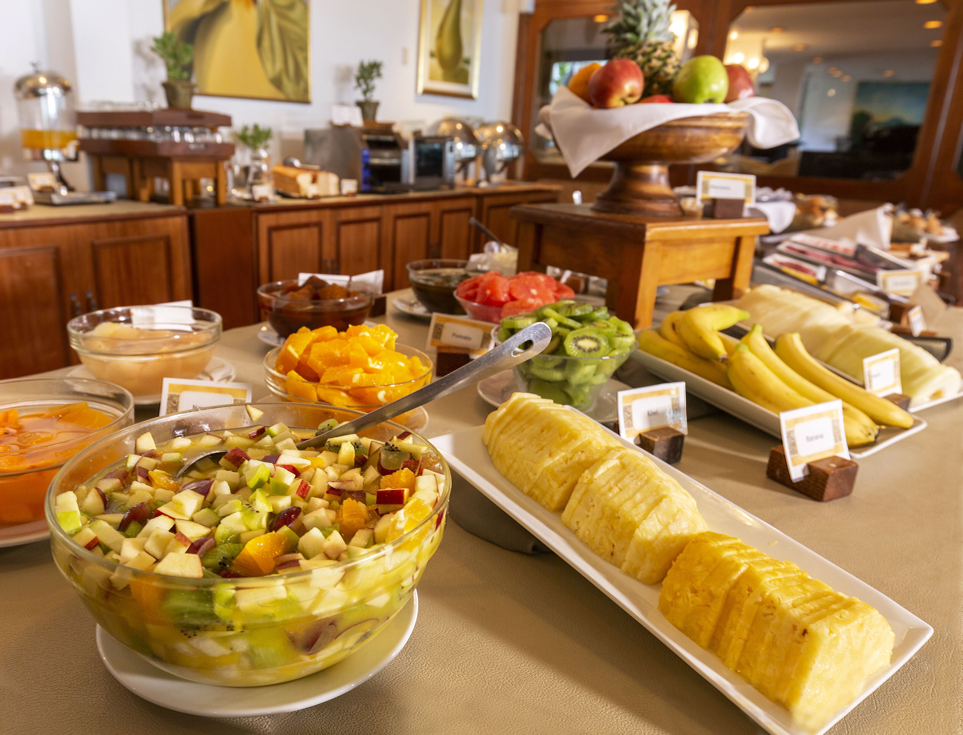 Un bufé con diversas frutas y un bol de ensalada de frutas.