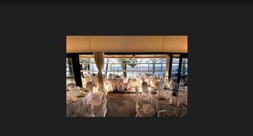 Un salón de banquetes interior con mesas redondas, manteles blancos y sillas.