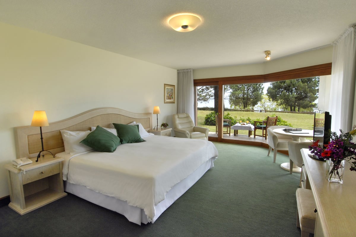 A hotel room with a large bed, two bedside tables, a desk, and a chair. There is a window with a view of the outdoors.