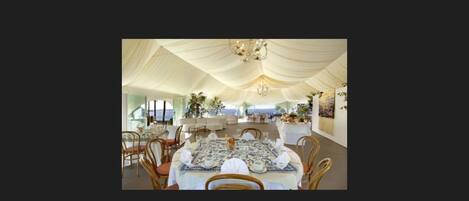 An indoor dining area with tables set for a meal, a chandelier, and a view of the sea.