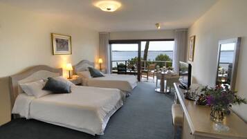 A hotel room with two beds, a TV, a desk, and a balcony with a view of the sea.