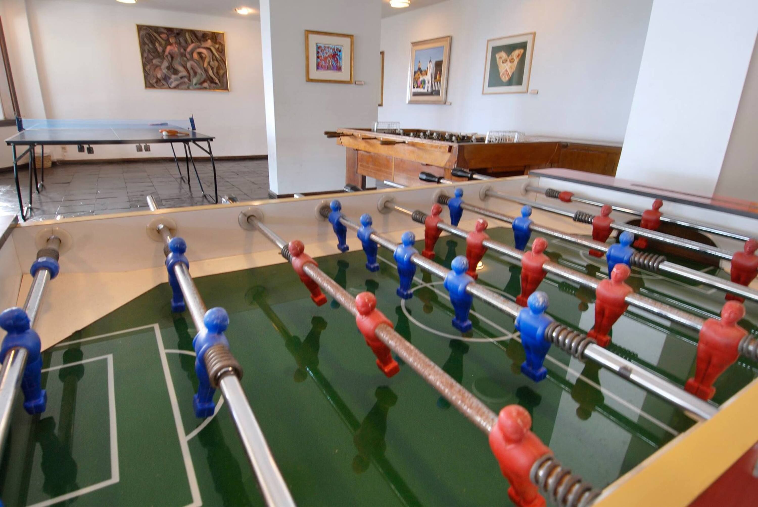 A room with a foosball table, a ping pong table, and a foosball table in the background.