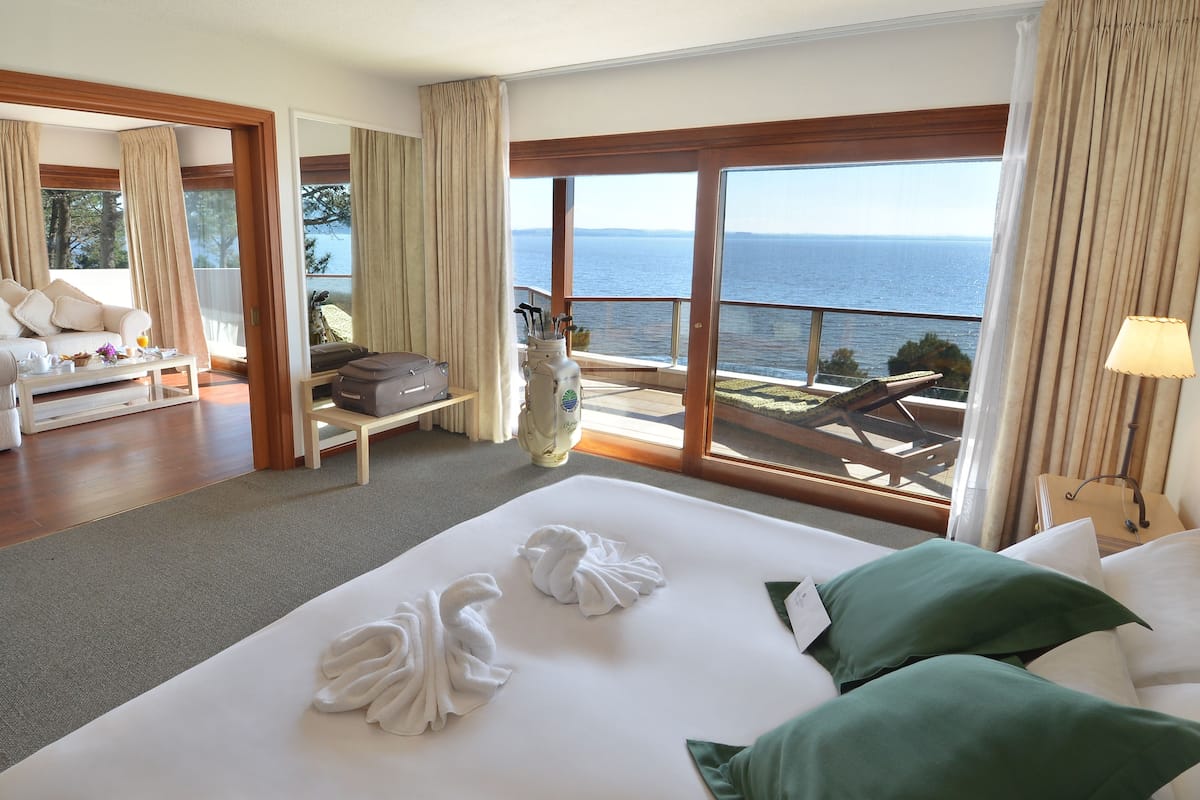 A hotel room with a large bed, a sofa, a coffee table, and a view of the sea.