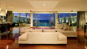 A modern living room with a large sofa, a dining area with chairs, and a view of a pool and sunset. - C151 Dreamland (Pecatu)