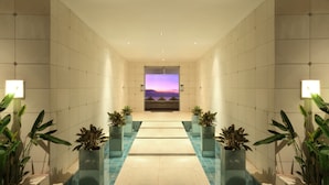 A hallway with a view of a sunset over the sea, potted plants, and a tiled floor. - C151 Dreamland (Pecatu)