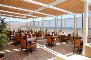 An outdoor dining area with tables and chairs, large windows, and a view of the beach. - Diego de Almagro Arica (Arica)