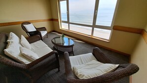 Una habitación con muebles de mimbre, incluyendo un sofá y sillones, una mesa de vidrio y un ventanal con vistas a la playa.