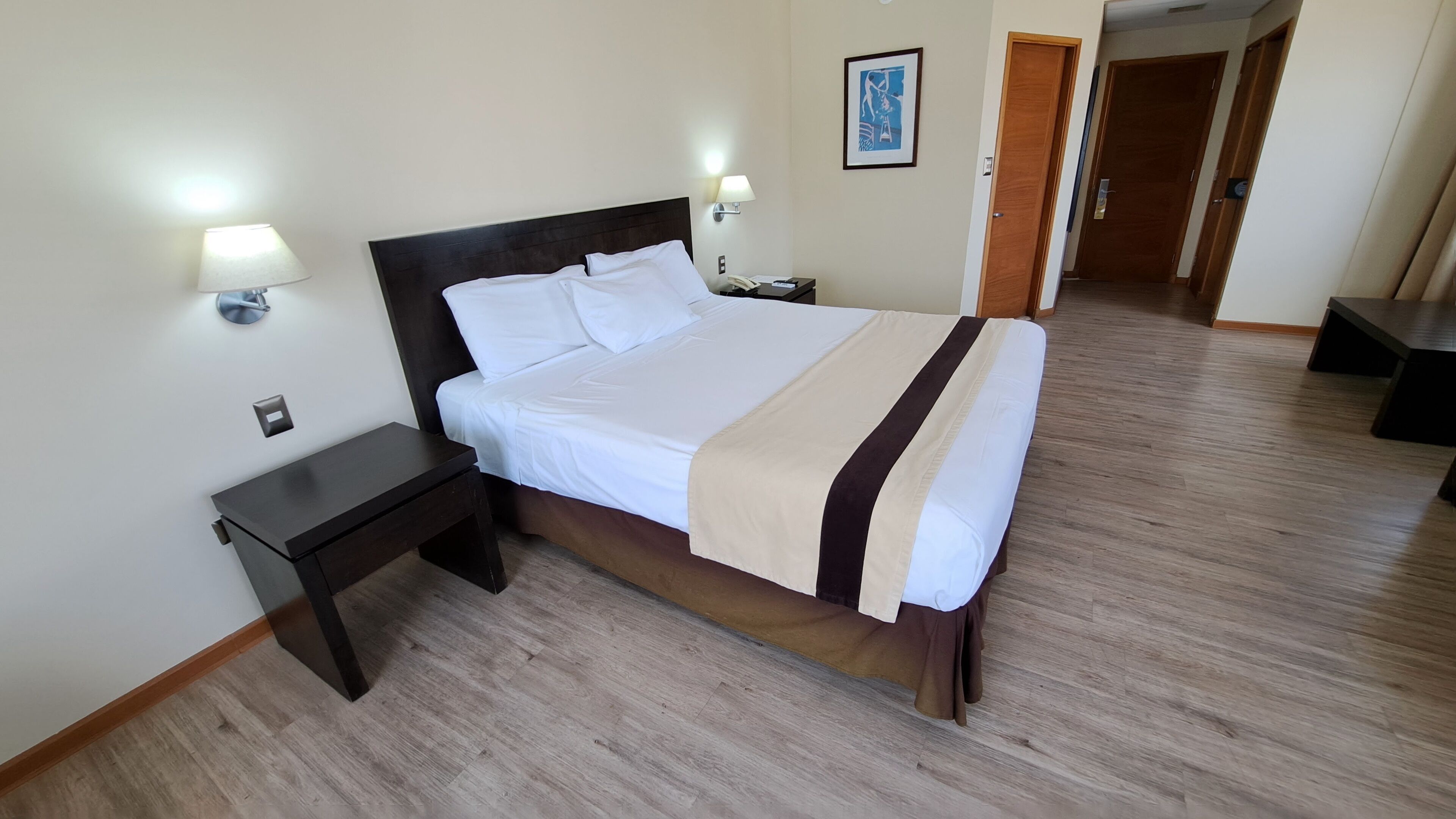 A hotel room with a large bed, bedside tables, a lamp, and a painting on the wall.