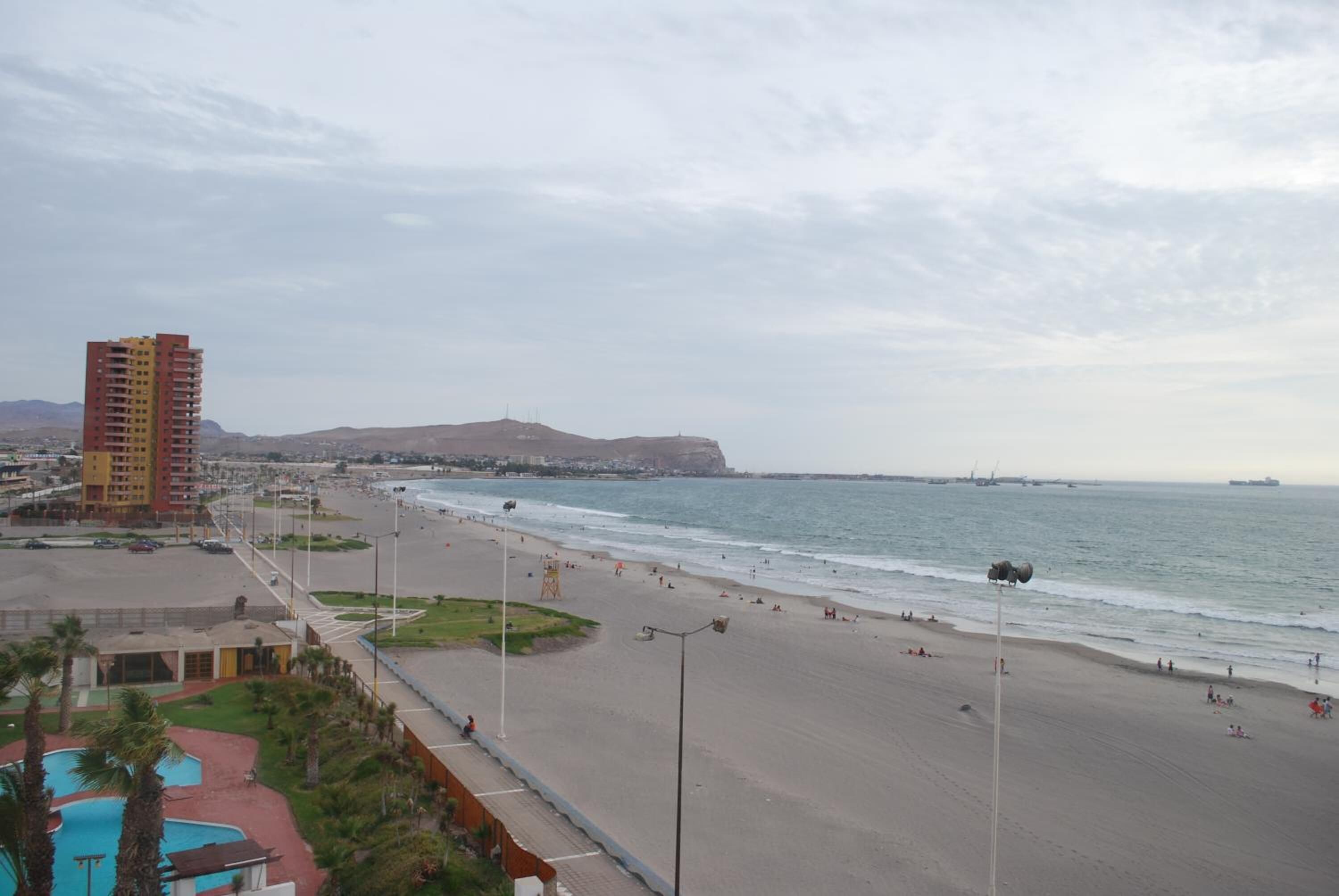 Una playa con un edificio alto, una piscina y una vista despejada del océano.
