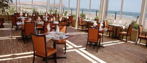 Un restaurant doté de tables et de chaises disposées dans un espace vaste, avec de grandes fenêtres donnant sur la plage.