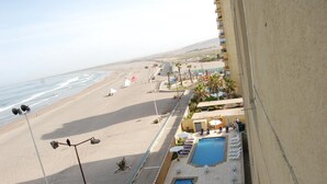 Un complejo turístico en la playa con piscina, sillones de descanso y sombrillas.