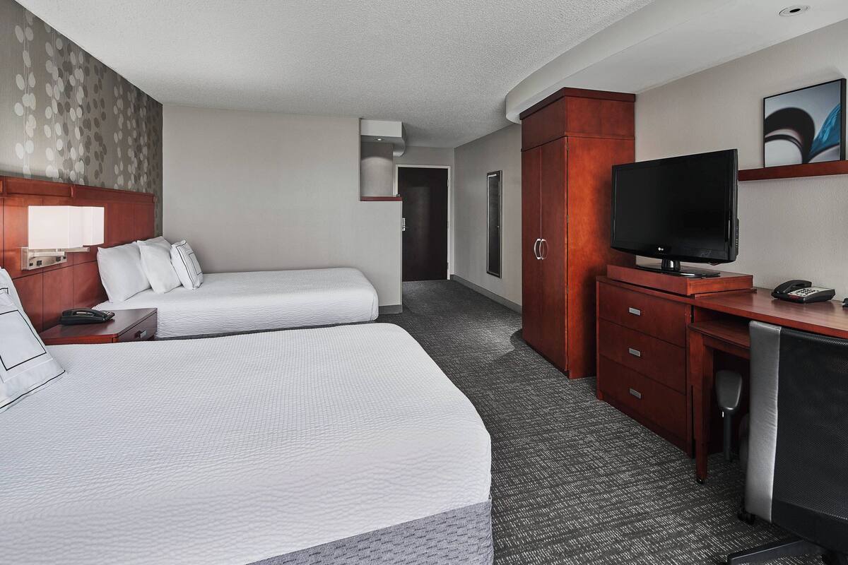 Une chambre d’hôtel avec deux lits, un bureau, une télévision et une armoire.