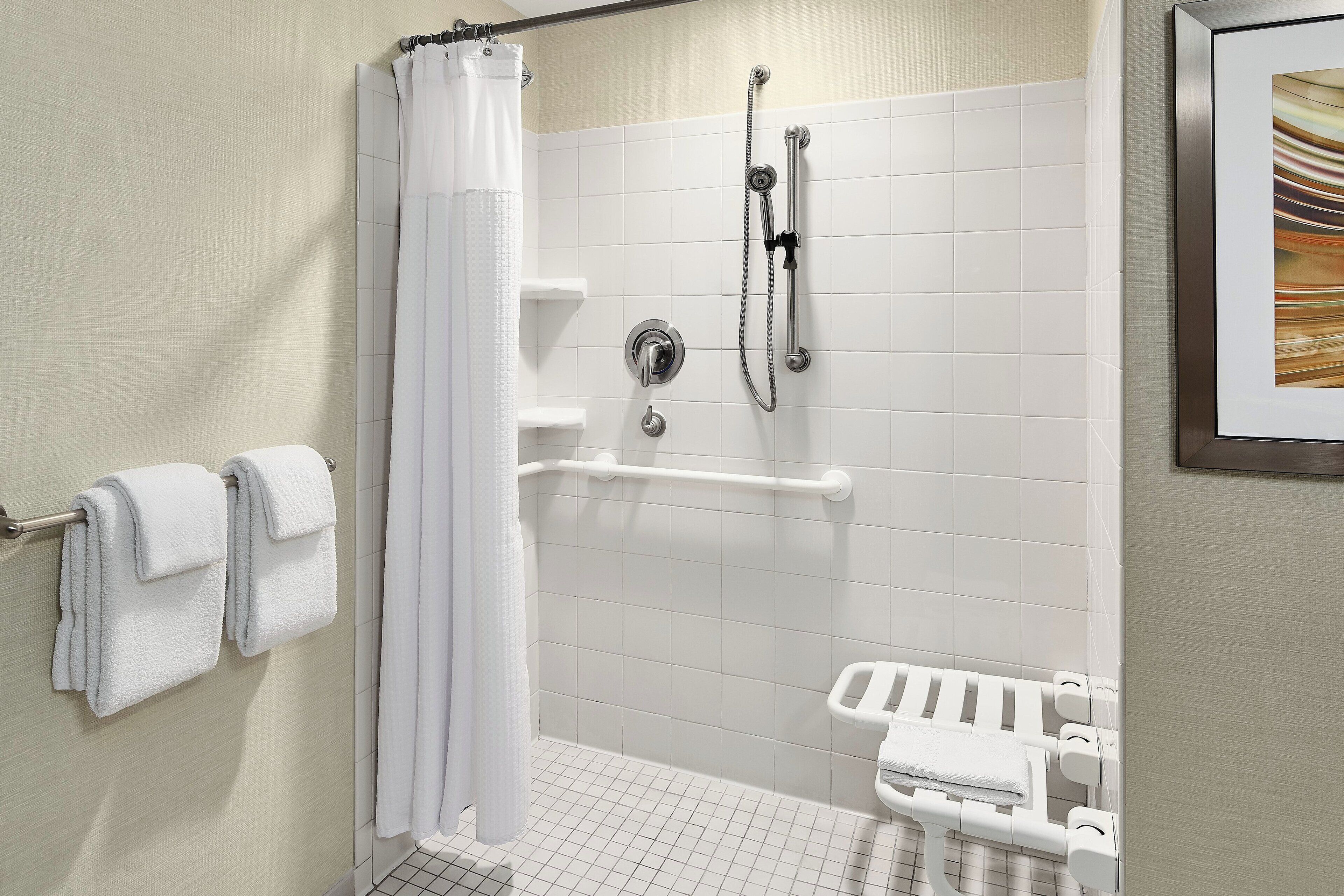 Een moderne badkamer met een douche, toilet met handgrepen en een handdoekrek.