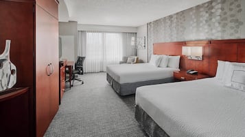 A hotel room with two beds, a desk, a chair, a wardrobe, and a large window with curtains.