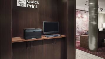Um balcão de recepção com uma impressora e computador, bancada de madeira e uma placa com a inscrição 'Quick Print'.