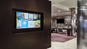 A modern hotel lobby with a digital display, seating area, and a flat-screen TV mounted on the wall. - Courtyard by Marriott Shreveport-Bossier/Louisiana Boardwalk (Bossier City)