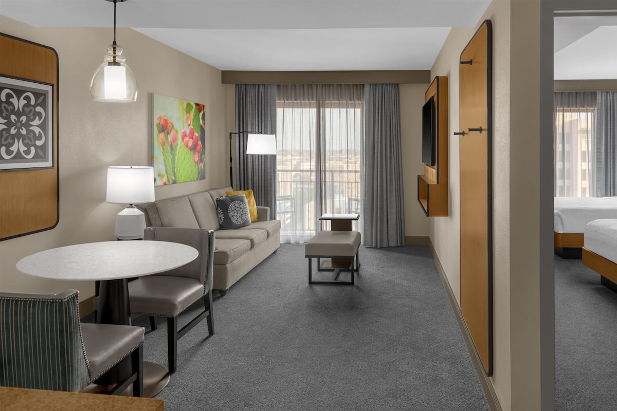 A hotel room with a sofa, a round table, a small table, a bench, a TV, and a bed.