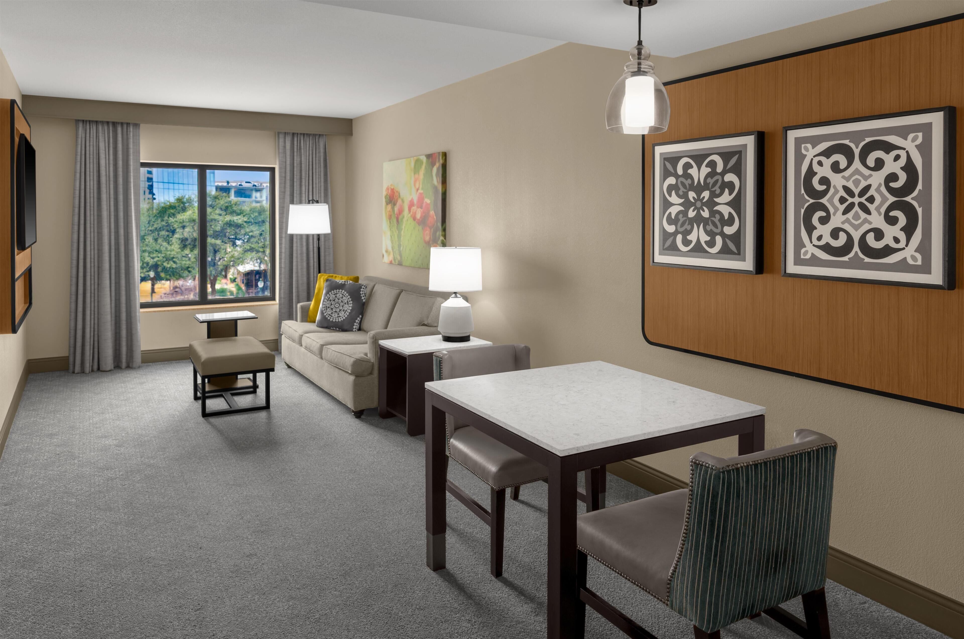 Habitación de hotel con sofá, una mesa de comedor, una silla, una lámpara y dos cuadros en la pared.