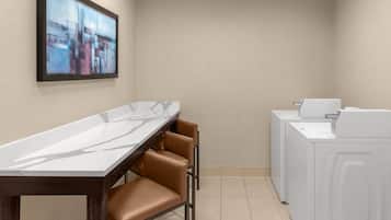 A modern kitchen with a marble countertop, brown leather chairs, and a white washing machine.