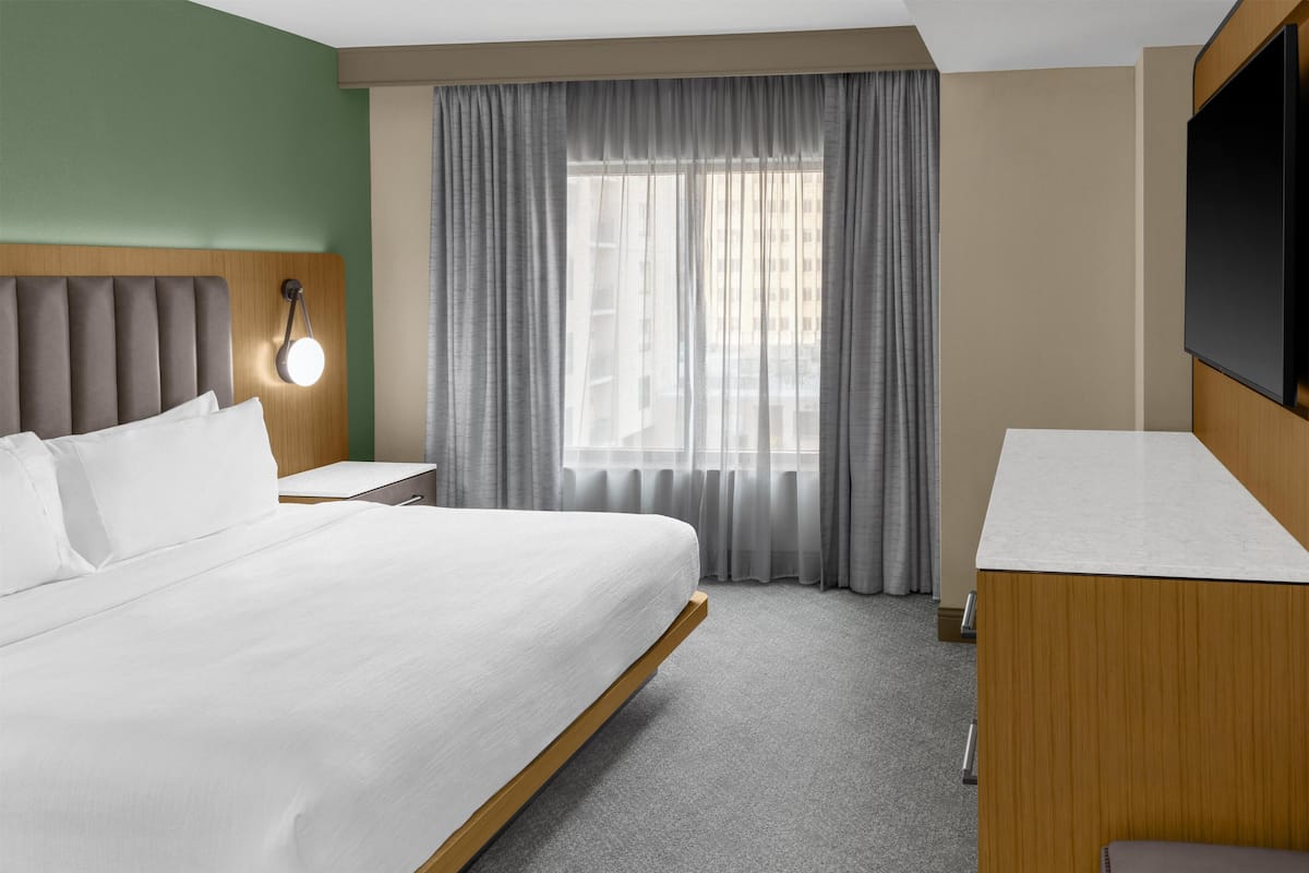 A hotel room with a bed, a bedside table, a TV, and a window with curtains.