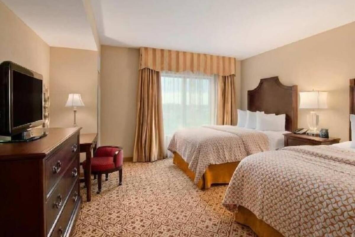 A hotel room with two beds, a TV, a dresser, and a window with curtains.
