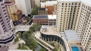 A high-rise building with a swimming pool, a river, and surrounding greenery. - Embassy Suites San Antonio Riverwalk-Downtown (San Antonio)