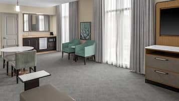 A hotel room with a kitchenette, a dining area with a table and chairs, a seating area with two chairs, a large window with curtains, and a television.