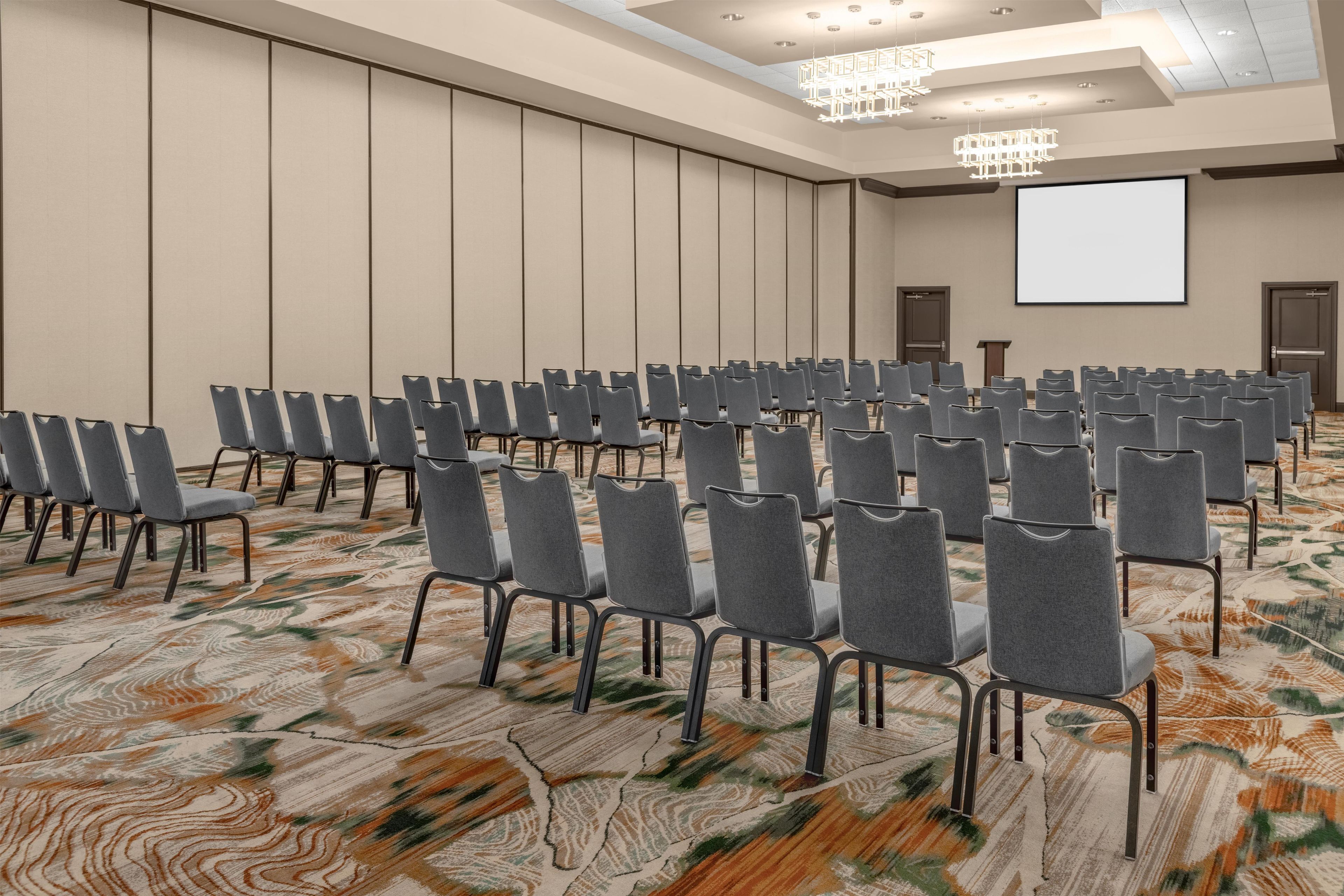 A conference room with rows of chairs, a projector screen, and a patterned carpet.