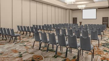 A conference room with rows of chairs, a projector screen, and a patterned carpet.