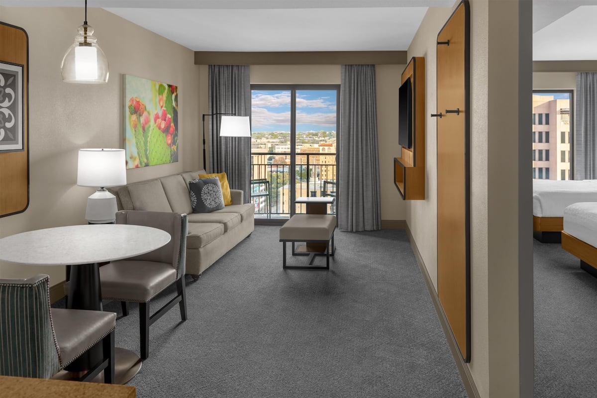 A hotel room with a balcony, a sofa, a dining table, and a bed.