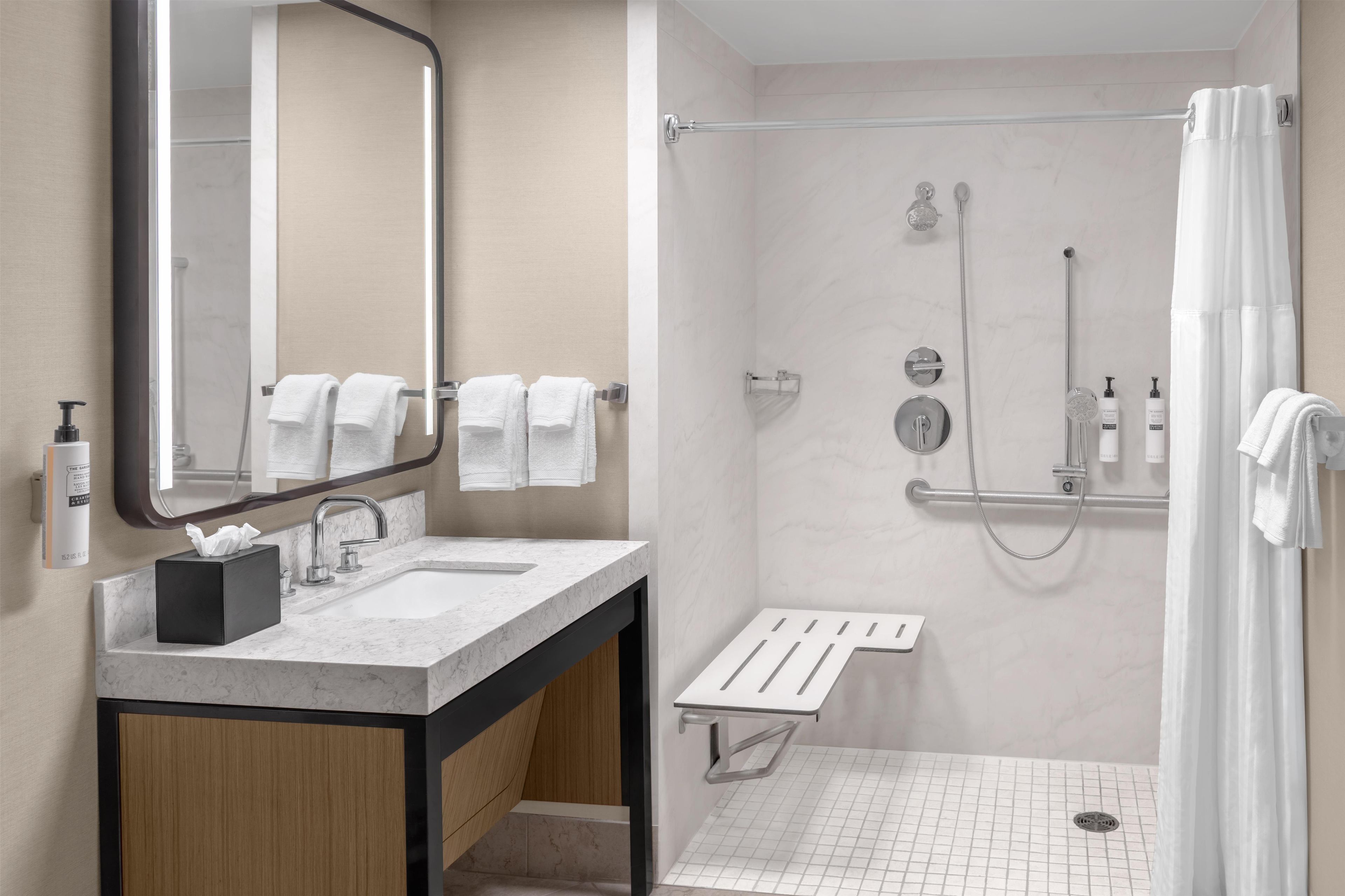 Une salle de bain moderne avec un lavabo en marbre, un grand miroir, une douche avec une porte en verre et un porte-serviettes.