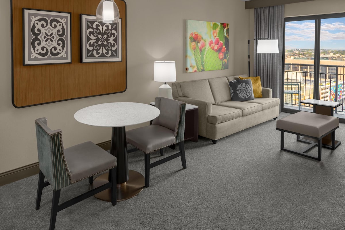 A hotel room with a round table, two chairs, a sofa, a small table, and a balcony with a view.