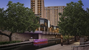 A riverside hotel with a boat dock, stone walls, and modern buildings in the background. - Embassy Suites San Antonio Riverwalk-Downtown (San Antonio)