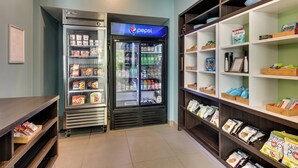 A self-service beverage station with a Pepsi refrigerator, snack shelves, and a counter with magazines.